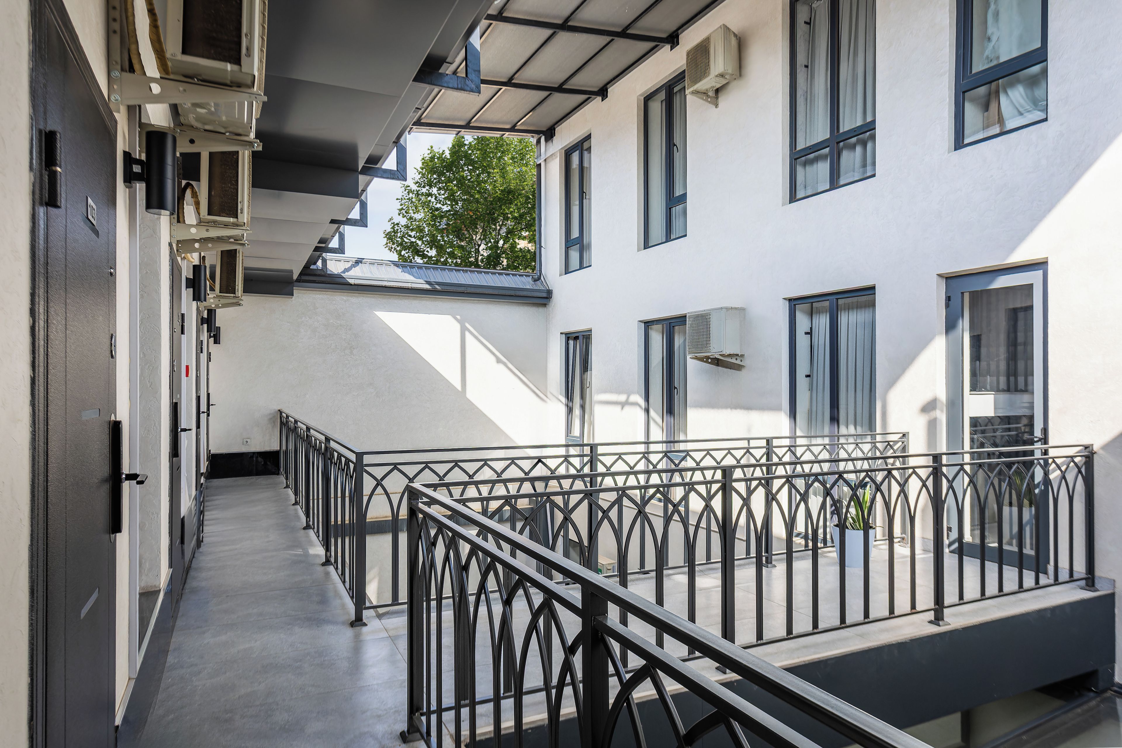 Un couloir avec une rambarde en métal, un escalier et un bâtiment doté de nombreuses fenêtres et de plusieurs unités de climatisation.