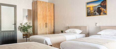 Habitación de hotel con tres camas, un armario de madera, una puerta con vidrio esmerilado y un cuadro con una escena costera.