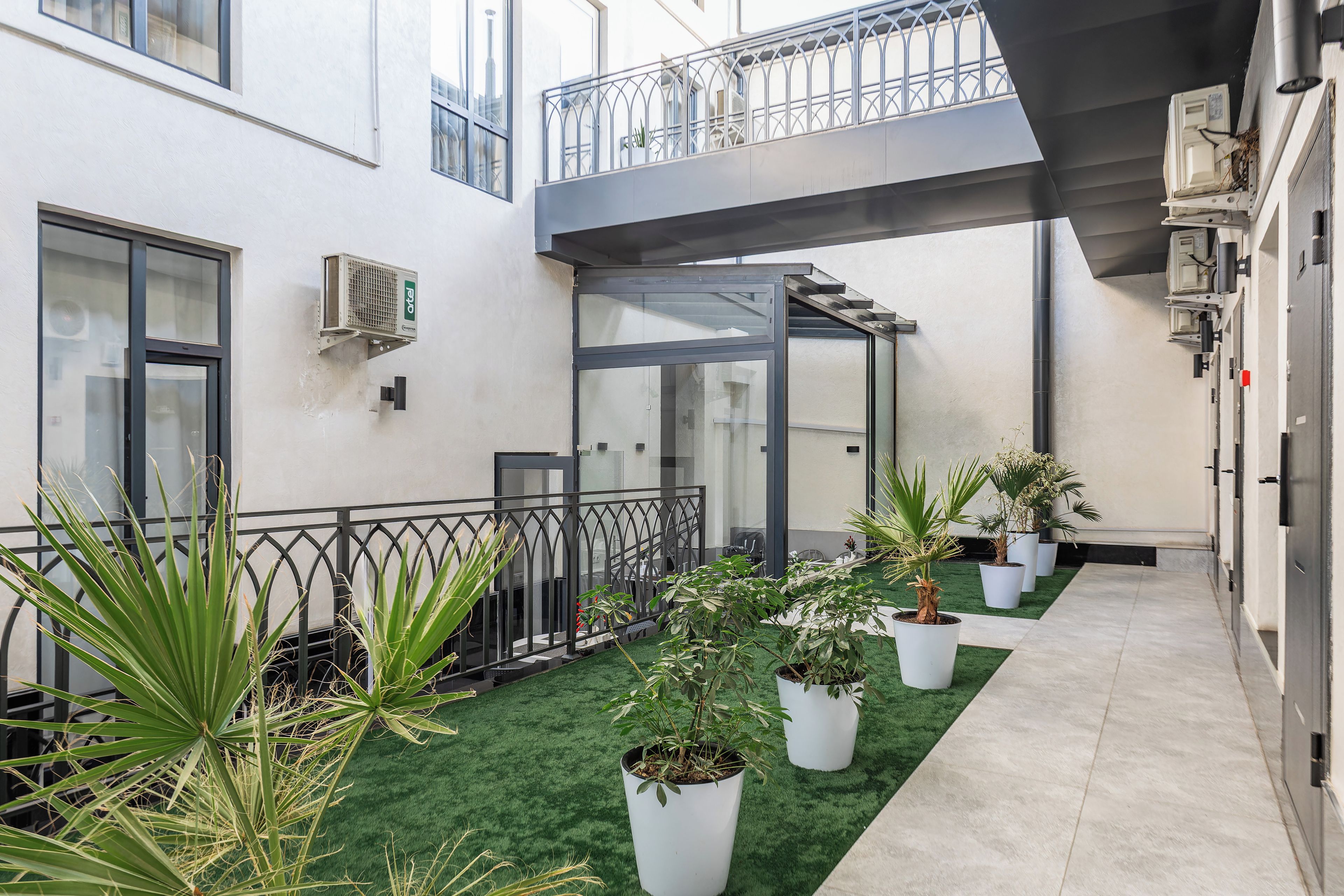 A modern building with a covered outdoor area, artificial grass, and potted plants.