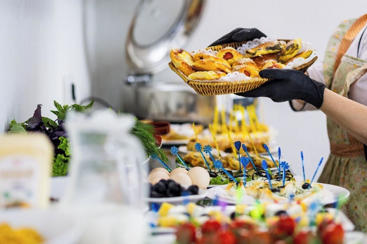 Een buffet met diverse gerechten en een persoon die een mand met gebak vasthoudt.