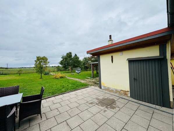 A patio area with a table and chairs, a garden with a lawn and trees, and a building with a garage. - Vacation home unterm Kohnstein (Nordhausen)