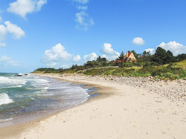 A beach with a house on a hill, clear skies, and waves. - 4 Person Holiday Home in Gilleleje (Gilleleje)
