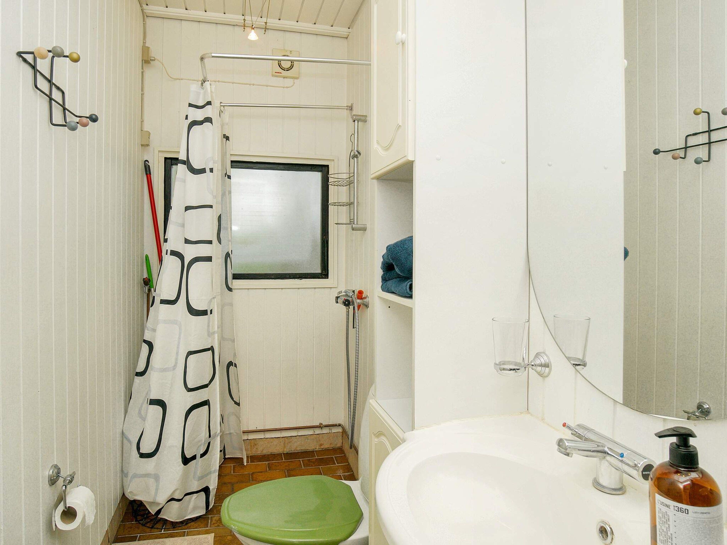 Une petite salle de bain avec des toilettes, un lavabo et une douche. On y trouve un porte-serviettes et un miroir.