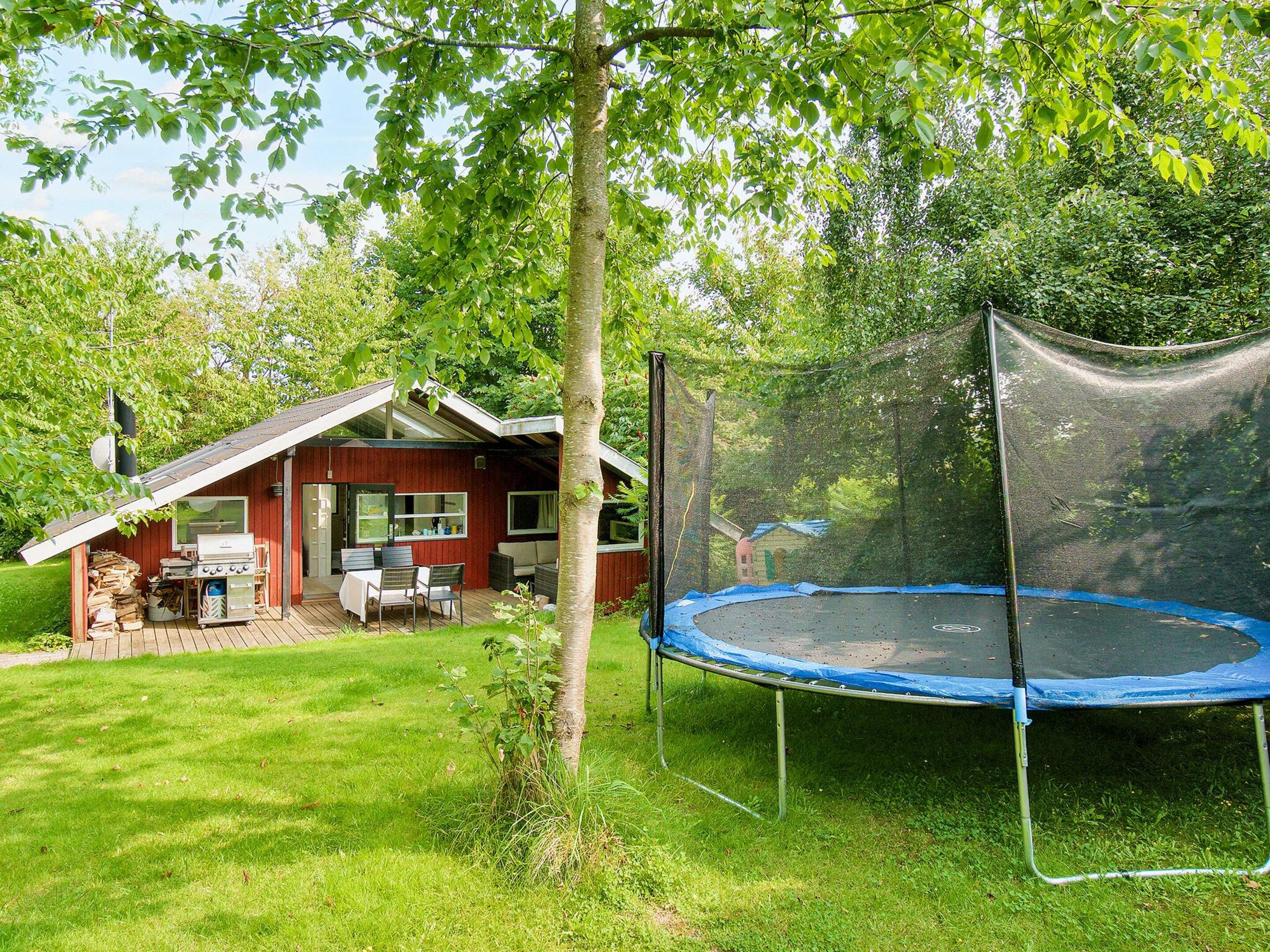 A wooden house with a covered patio, a trampoline, and a lawn.