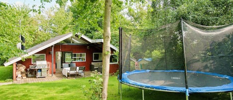A wooden house with a covered patio, a trampoline, and a lawn.