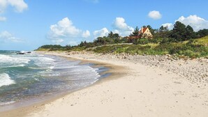Ein Strand mit einem Haus auf einem Hügel, Wellen und einem klaren Himmel.