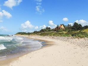 A beach with a house on a hill, waves, and a clear sky. - 4 Person Holiday Home in Gilleleje (Gilleleje)