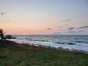 A coastal landscape with a wooden fence, grassy area, and the ocean.