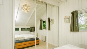 Ein Schlafzimmer mit einem raumhohen Spiegelkleiderschrank, einem Bett mit weißer Bettwäsche, einem Holz-Kopfteil und einer Deckenleuchte.