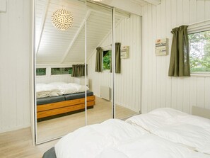A bedroom with a mirrored wardrobe, a bed with white bedding, a wooden headboard, and a ceiling light fixture. - 4 Person Holiday Home in Gilleleje (Gilleleje)