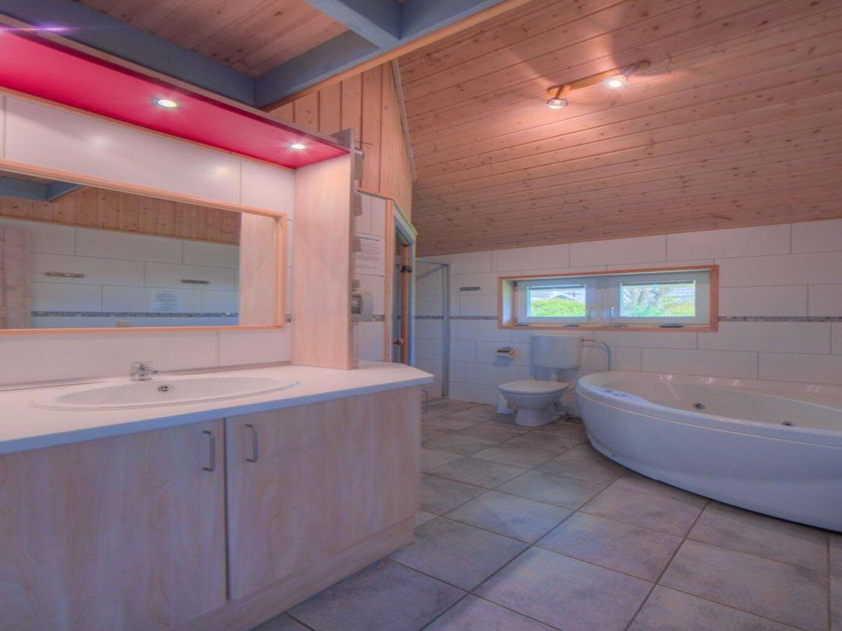 A modern bathroom with wooden ceiling, a large bathtub, two sinks, and a window.
