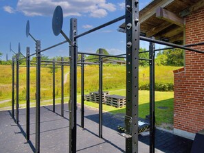 Une structure métallique abritant une salle de sport, dotée d’un toit et entourée d’un bâtiment en briques et d’un terrain herbeux.