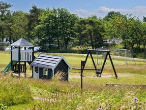 Une aire de jeux avec un toboggan, une balançoire et une petite maison de jeux.