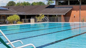A swimming pool with clear blue water, surrounded by a brick building with a metal roof and solar panels. - 6 Person Holiday Park Home in Gilleleje (Gilleleje)