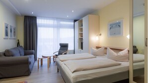 A modern hotel room with a bed, a sofa, a chair, a small table, and a wardrobe. - Ferienwohnung im Aparthotel Seepanorama (Mirow)