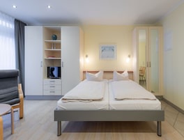 A double bed with a wooden frame, a bedside table, a chair, a wardrobe, and a television.