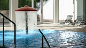 A swimming pool with a water feature, indoor seating, and large windows. - Ferienwohnung im Aparthotel Seepanorama (Mirow)