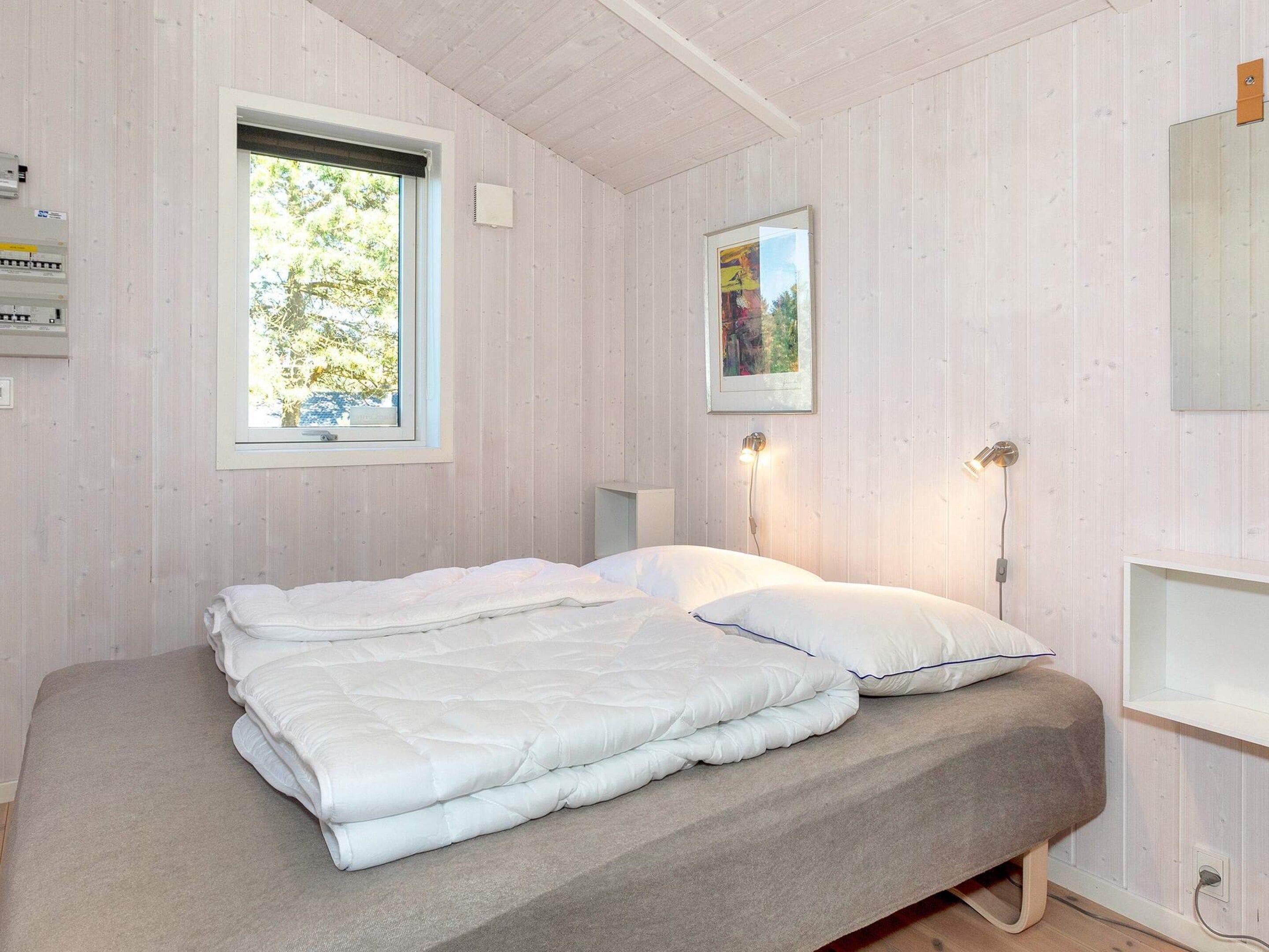 Un dormitorio con una cama, una ventana, una lámpara de pared y un cuadro enmarcado.