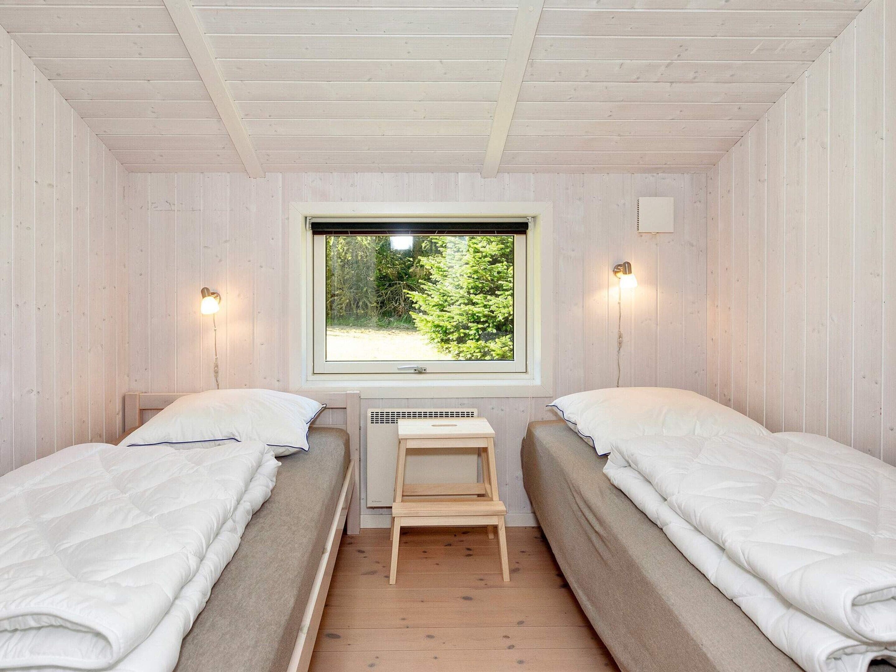 A room with two beds, a window with a view of greenery, and a small table.