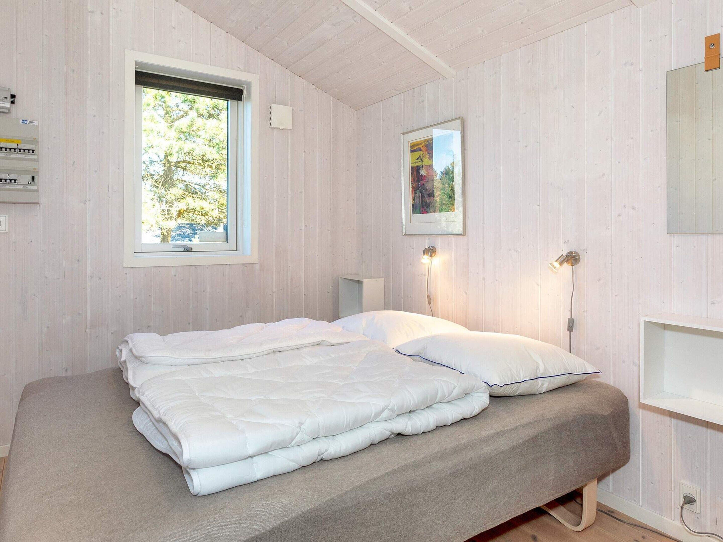 A bedroom with a bed, a window, a wall-mounted light, and a framed picture.