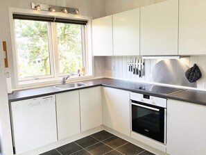 Une cuisine moderne avec des meubles blancs, un plan de travail noir, un lave-vaisselle et une fenêtre donnant sur les arbres.