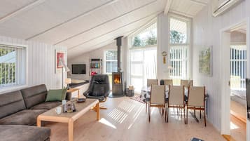 Uma sala de estar ampla com lareira, um sofá, uma mesa de centro e um espaço de jantar com cadeiras.