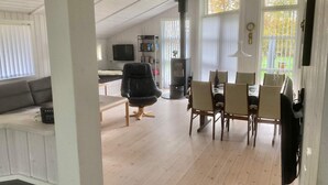 Uma sala de estar ampla com uma mesa de jantar, cadeiras, uma poltrona de couro preto, estante, televisão e lareira.