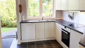 Uma cozinha moderna com armários brancos, bancada preta, forno embutido e janela com vista para o verde.