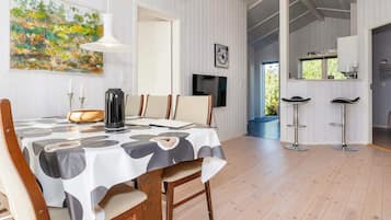 Un comedor con una mesa dispuesta para cuatro, sillas de madera, una lámpara colgante moderna y un cuadro en la pared.