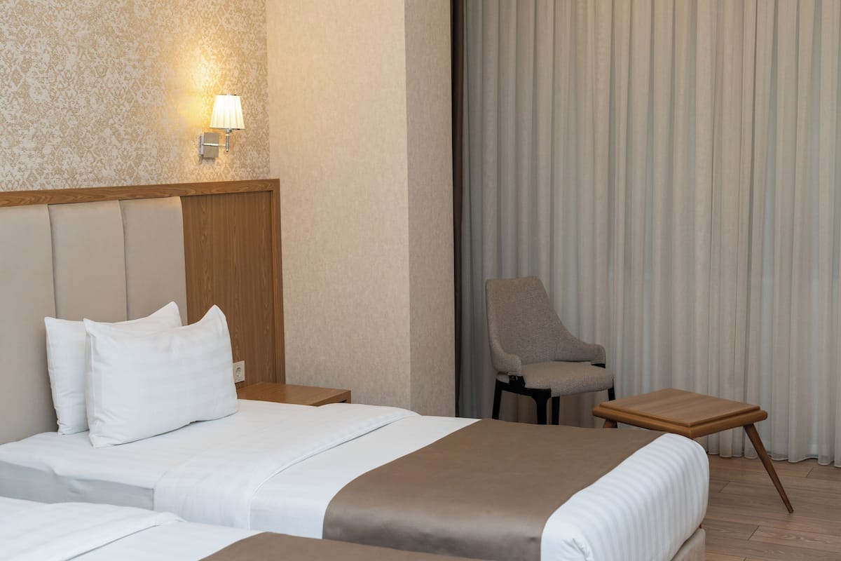 A hotel room with a large bed, a nightstand, a chair, and a small wooden table.