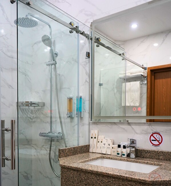 Une salle de bain moderne avec une douche à parois de verre, des murs en marbre, un comptoir en granit et un panneau indiquant qu'il est interdit de fumer.
