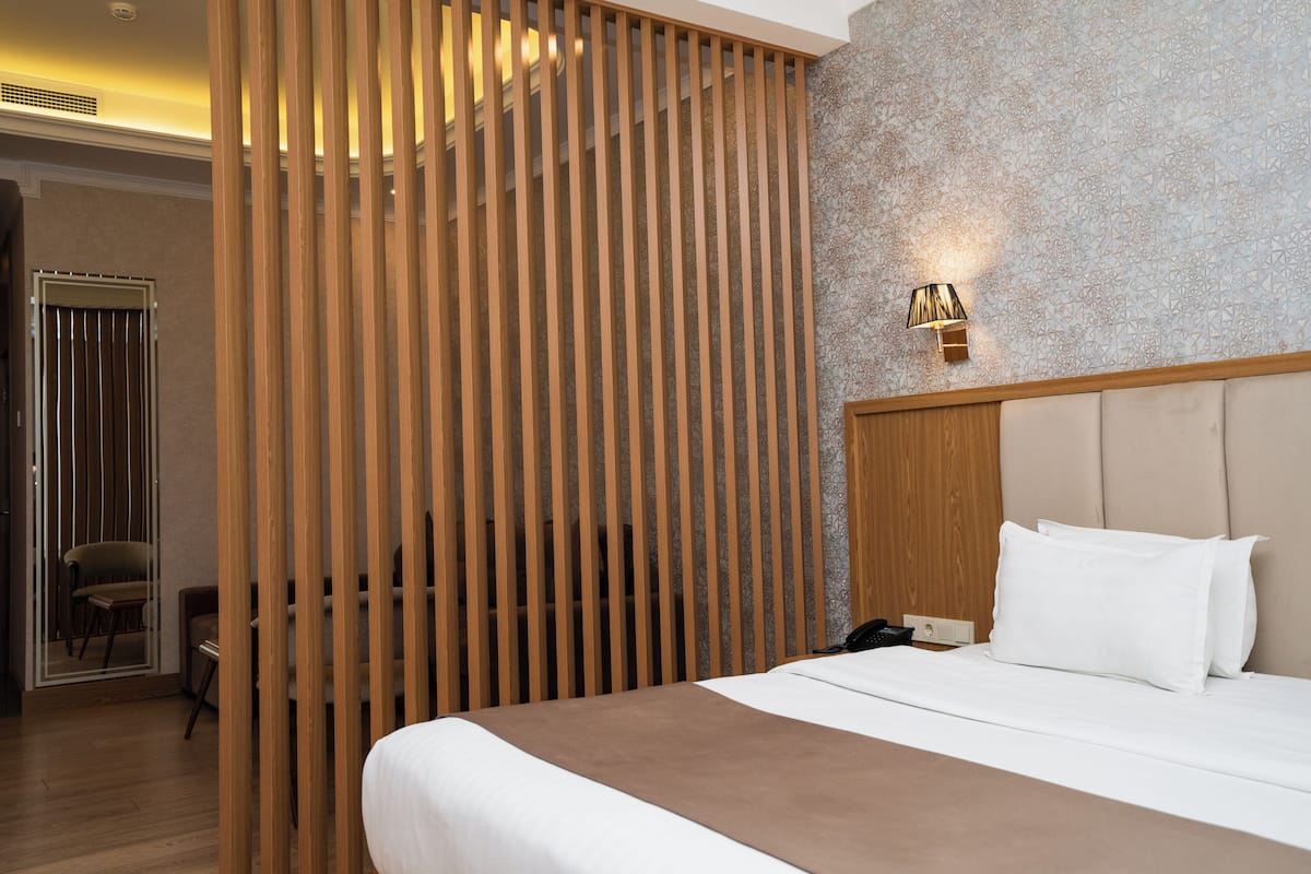 A hotel room with a large bed, a wooden partition, a wall-mounted lamp, and a chair.