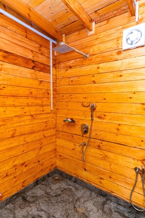 A wooden cabin with a shower area, including a showerhead, a handheld shower, and a wall-mounted fan. - Ourem Palace Luxury Beach Huts (Canacona)