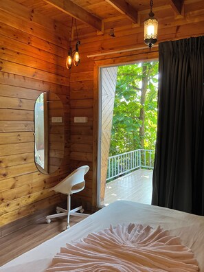 A wooden cabin room with a bed, a white chair, a mirror, and a balcony with a railing. - Ourem Palace Luxury Beach Huts (Canacona)