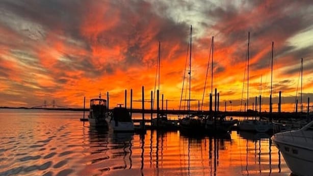 Een jachthaven in de zonsondergang met aangemeerde boten, rustig water en een brug op de achtergrond.