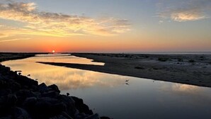 Een zonsondergang boven een rustig wateroppervlak met een rotsachtige kustlijn.