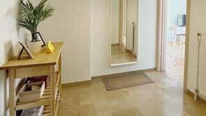A spacious hallway with a wooden desk, a potted plant, a mirror, and a door leading to a kitchen area. - Blue Coast Residence Glyfada (Glyfada)