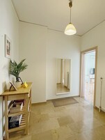 A spacious hallway with a wooden desk, a potted plant, a mirror, and a door leading to a kitchen area.