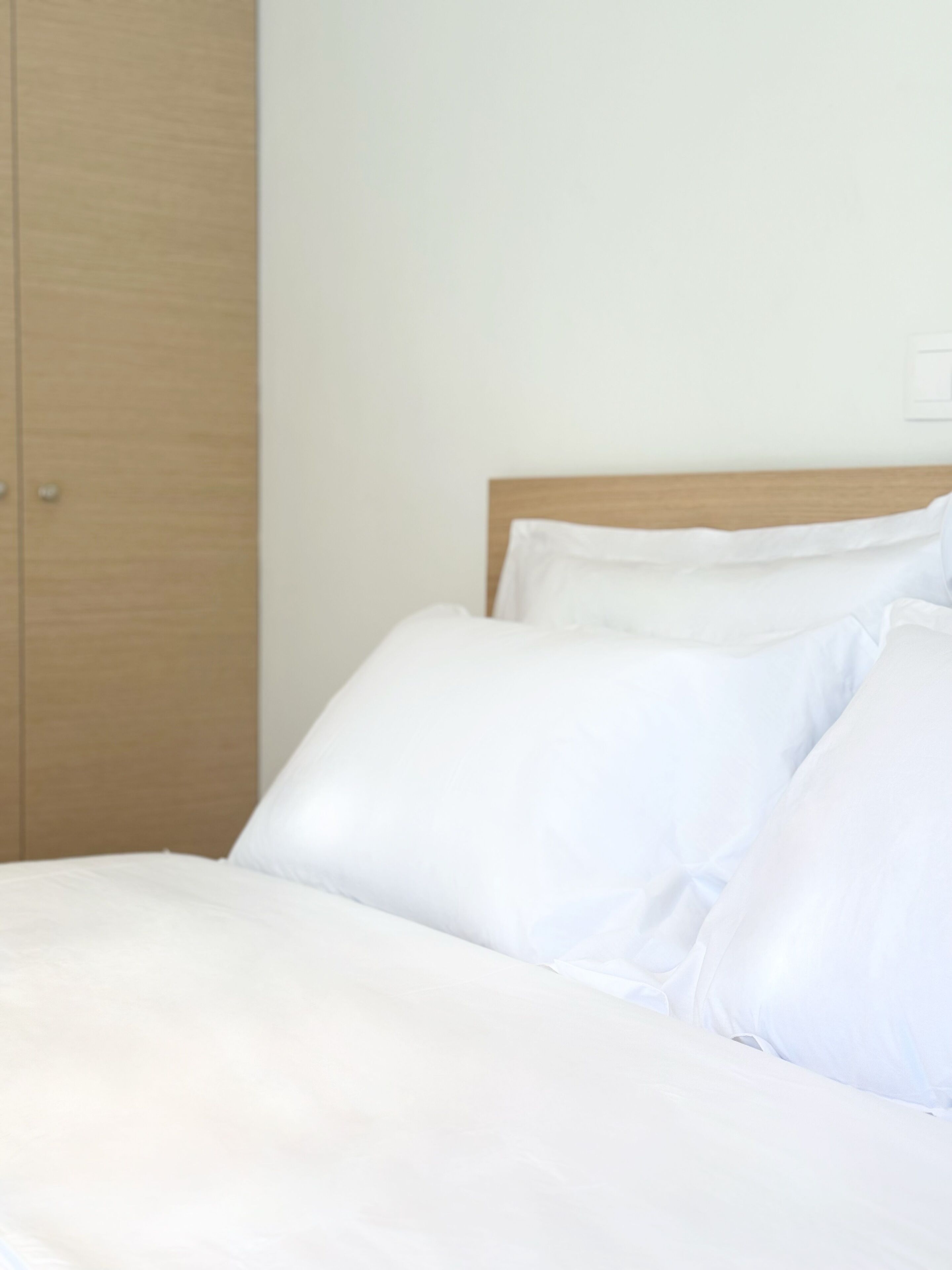 Una cama con ropa blanca en una habitación con cabecera y armario de madera.