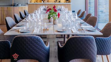 A dining area with a long table set for a meal, surrounded by upholstered chairs.
