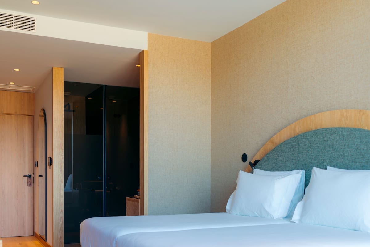 Ett modernt hotellrum med en säng i trä, en rymlig klädkammare och ett badrum med en dusch av glas.