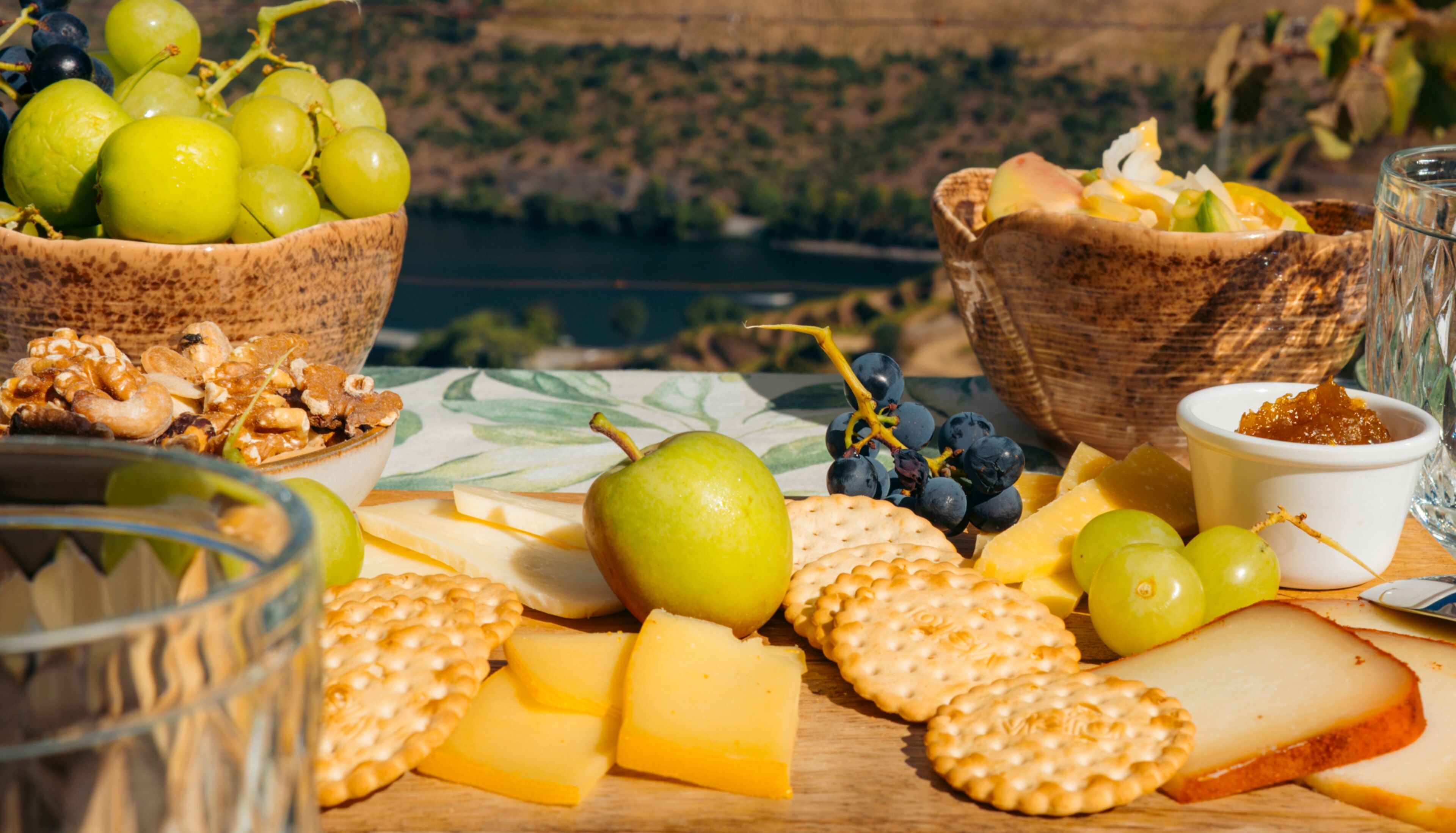 A table with cheese, crackers, grapes, nuts, and a glass of water.