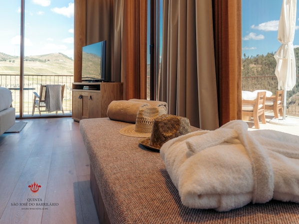 A hotel room with a large window, a sofa, a TV, and a view of the outdoors. - Quinta São José do Barrilario (Armamar)