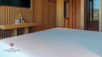 Una habitación de hotel moderna con un panel de pared de madera, un televisor montado, una estantería de madera con vasos y botellas, y una cama.