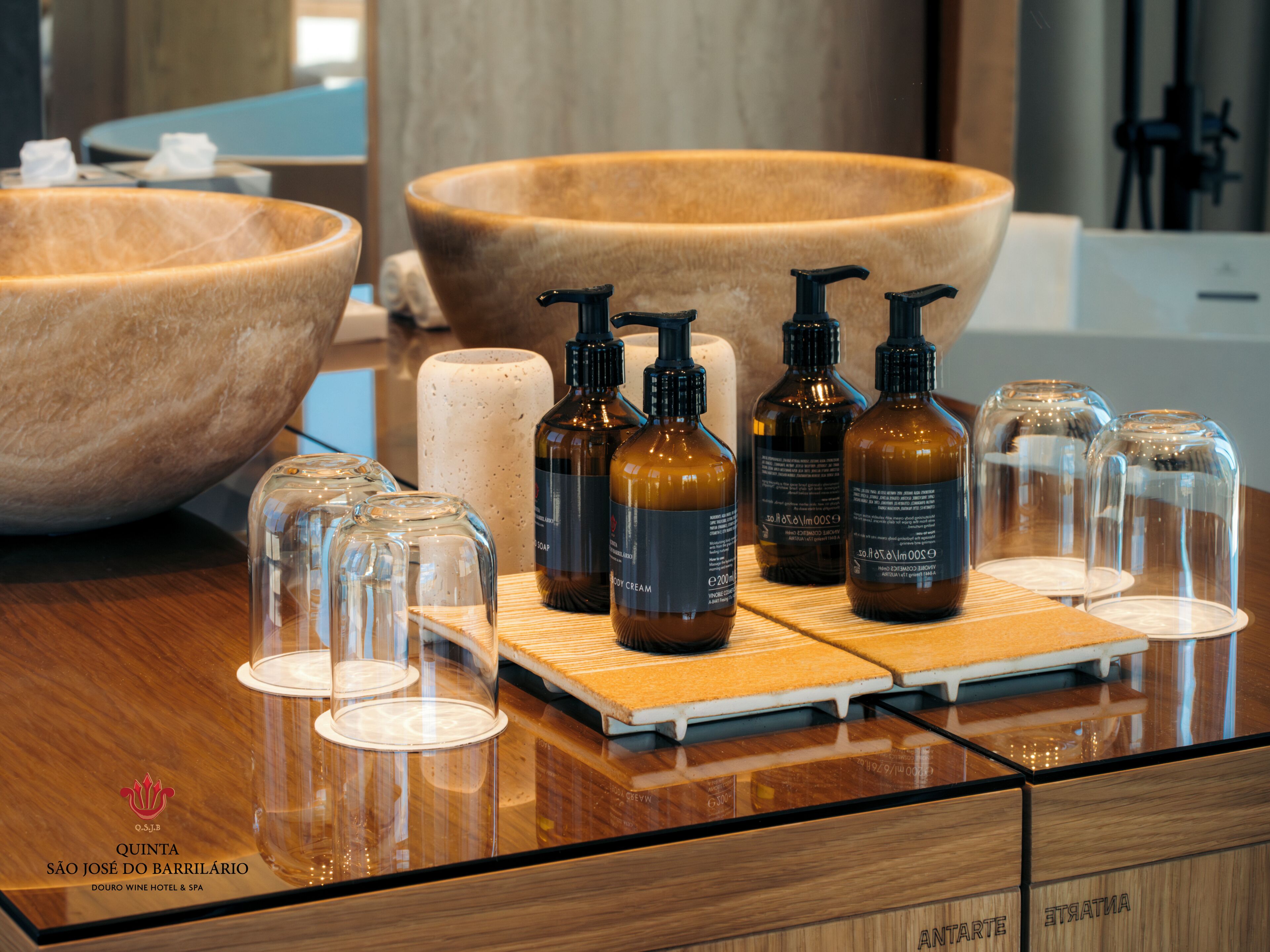 A bathroom vanity with a large wooden bowl sink, several bottles of soap, and clear glass containers.