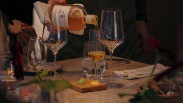 A wine tasting event with several wine glasses on a table, a bottle of wine being poured, and a wooden board with a small dish.