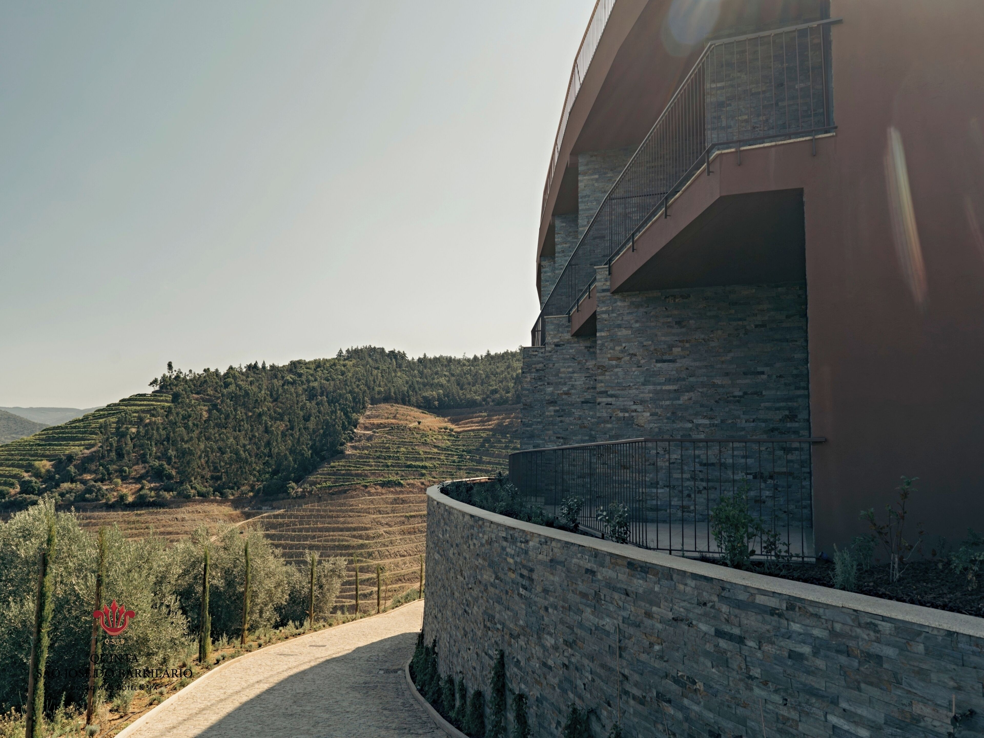 A modern building with a stone facade and a curved balcony overlooking terraced vineyards.