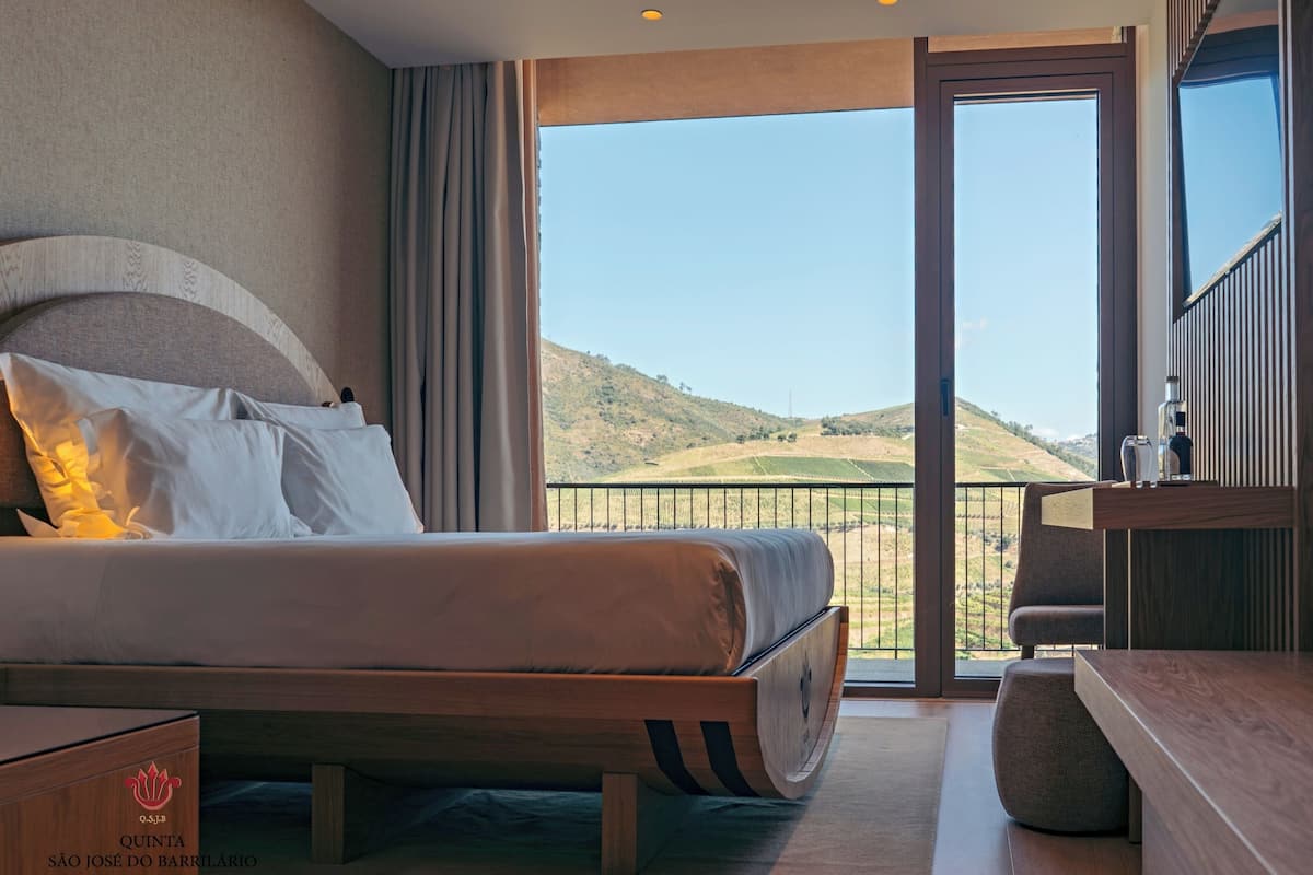 Ett hotellrum med en stor säng, en balkong med utsikt över landskapet och en minibar.