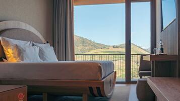 A hotel room with a large bed, a balcony with a view of the countryside, and a minibar.