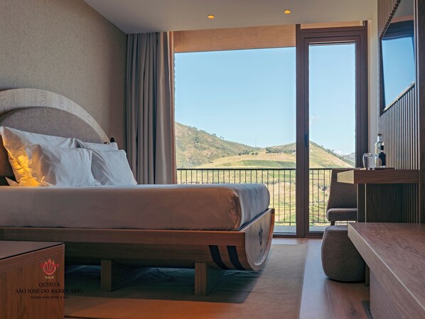 A hotel room with a large bed, a balcony with a view of the countryside, and a minibar. - Quinta São José do Barrilario (Armamar)